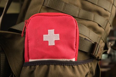 Üzerinde beyaz haç olan kırmızı bir ilk yardım çantası Molle sistemli askeri bir zeytin çantasının cebinde.