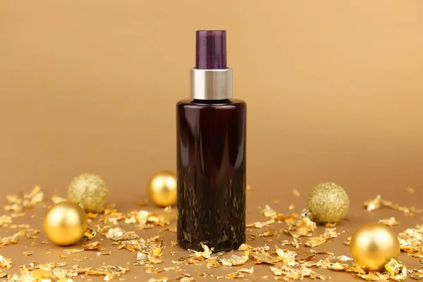 Brown cosmetic spray bottle, gold Christmas balls, pieces of gold paper on golden background. Body or hair natural oil, skincare, sanitizer, deodorant, moisturizer, micellar water. Mockup, front view