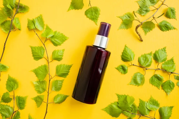 Mockup of brown cosmetic spray bottle and birch leaves on yellow background. Body mist, skincare, suntan oil, sanitizer, deodorant, moisturizer, micellar water. Cosmetic blank bottle container. Front