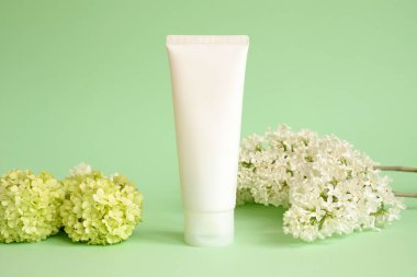 Sahte beyaz sıkma şişe kozmetik tüpü, yeşil viburnum çiçekleri ve yeşil arka planda beyaz leylak çiçekleri. Şampuan, krem, jöle, cilt bakımı, güneş kremi, nemlendirici. Ön görünüm, boş tüp, şablon.