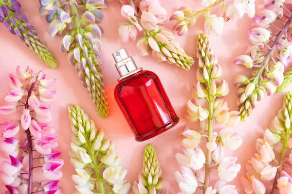 Perfume spray red bottle and pink lupine flowers on pink background. Front top view, summer flat lay, mockup.