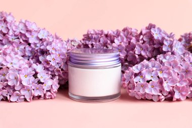 Mockup beyaz kavanoz metal kapaklı nemlendirici krem ve pembe arka planda leylak çiçekleri. Yakın çekim, yaz cilt bakımı kozmetik. Ürün markalaştırma, krem losyonu, nemlendirici. Ön görünüm.