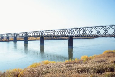 Güneşli bir sonbahar gününde nehirden geçen demiryolu köprüsü.