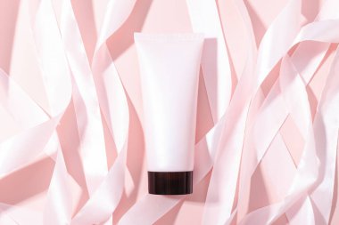 Pembe sıkma şişe kozmetik tüpü, siyah kapaklı ve pembe arka planda pembe altın kurdeleler, maket. Günlük krem, jöle, cilt bakımı, güneş kremi, nemlendirici. Ön manzara, boş tüp