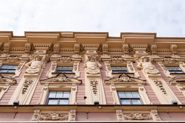 stock image Facade of light pink color historic house with beautiful windows, sculptures of men, floral decor. From bottom to top view.