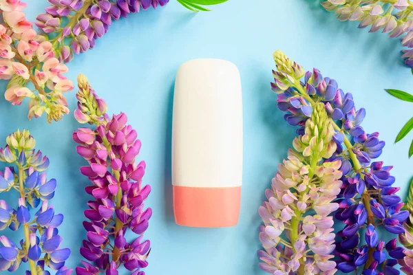 Mockup white cosmetic tube bottle with pink screw cap and multicolored lupine flowers a lot on blue background. Moisturizing cream, gel, skincare, sunscreen, moisturizer, front top view, mock-up.