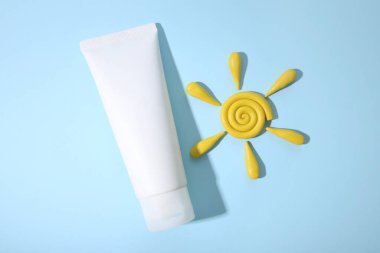 İlaç ya da kozmetik ürünlerini damgalamak için beyaz sıkılmış plastik tüp. Günlük krem, jöle, cilt bakımı. Kozmetik şişe kabı ve sarı plasticine model kil güneş mavi arka planda. Model