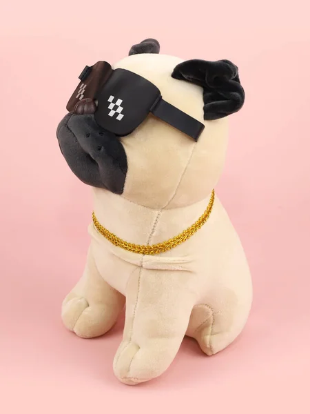 Plush soft beige black pug dog toy with sunglasses isolated on pink background. Three quarter portrait Diagonal snapshot.