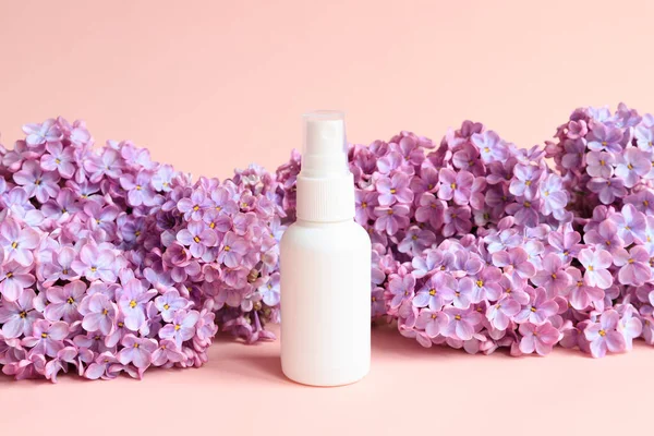 White cosmetic spray bottle and lilac flowers on pink background. Front view, mockup, template. Natural organic spa cosmetics and liquid antibacterial spray concept.