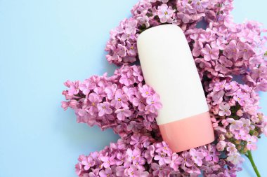 Mavi arka planda pembe vida kapaklı beyaz kozmetik tüp şişesi ve leylak çiçekleri. Vücut nemlendirici krem, jöle, cilt bakımı, güneş kremi, nemlendirici, losyon, ton düzeltmesi. Ürün markası