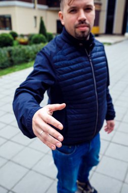 Kameraya bakarken, beyaz iş adamı 34 yaşında keçi sakallı bir adam sokakta el sıkışırken selam veriyor. Üç çeyrek boy yaşam tarzı portresi, dikey fotoğraf.