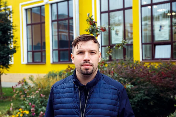 Young caucasian 34 years old man in blue jacket with goatee beard on yellow building. Looking at camera concentrated entrepreneur man, businessman. Waist up lifestyle business portrait, success