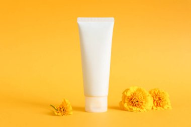 Beyaz krema tüpü ve sarı arka planda kadife çiçekleri. Kozmetik cilt ürünleri boş plastik paket. Beyaz markasız losyon şişesi, balsam, diş macunu maketi, ön manzara..