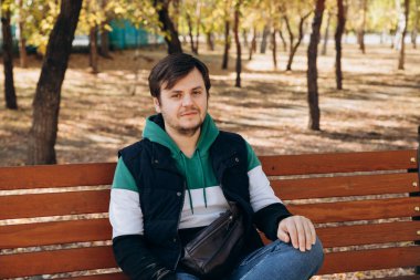 Kameraya bakıyorum. 34 yaşında, kazaklı ve kalın yelekli beyaz bir adam sonbahar parkında bankta oturuyor. Açık hava parkı, güneşli bir gün, belden yukarı yaşam tarzı portresi. Bekleme kavramı