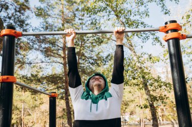 34 yaşında, beyaz, traşsız, spor salonunda barfiks çeken güneşli bir sonbahar gününde barlarda takılan sporcu olmayan bir adam. Açık hava parkı spor ekipmanları. Yaşam tarzı portresi.