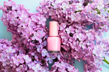 Pembe tırnak cilası küçük cam şişe ve mavi arka planda leylak çiçekleri. Profesyonel manikür konsepti. Mockup, ön görünüm.