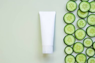 Taklit beyaz sıkma şişe kozmetik tüp ve yeşil arka planda taze doğranmış salatalık. Vücut kremi, jöle, cilt bakımı, güneş kremi, nemlendirici, diş macunu. Ön üst görünüm, boş tüp, şablon, düz uzanma