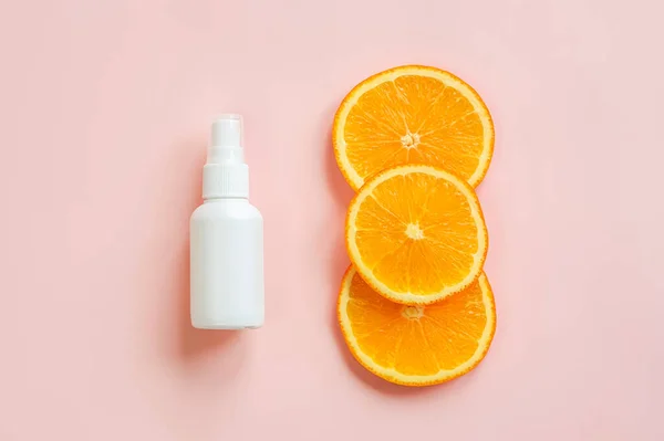 Mockup white cosmetic spray mini travel bottle and three sliced orange on pink background. Body mist, sanitizer, perfume, sunscreen oil with vitamin c. Front view, blank bottle, template.