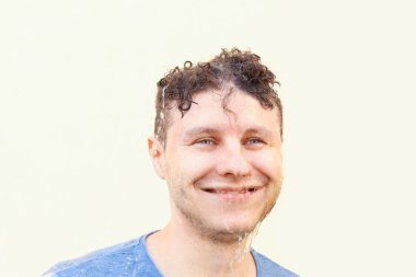 Islak Avrupalı beyaz erkek. Sarı arka planda düşen su jeti var. Yüzüne su damlıyor. Bakıyor ve gülümsüyor. Yağmur ve olumlu duygular, portre, ruh sağlığı, yaşam tarzı.