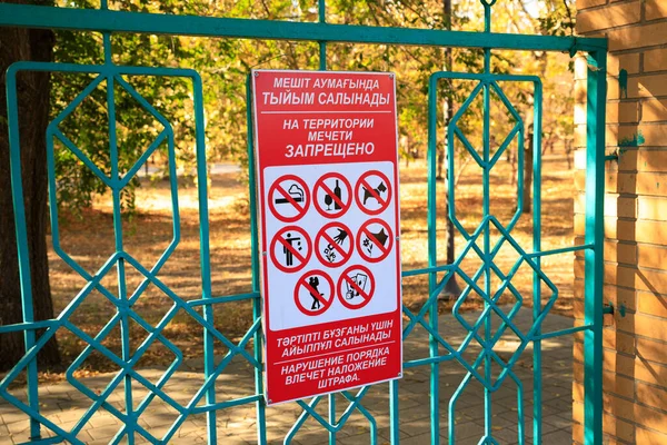 stock image Rules at entrance to courtyard of Mashkhur Jusup Central Mosque in Pavlodar. It is written: it is forbidden on territory of mosque. Violation of order entails fine. Fencing and autumn park.