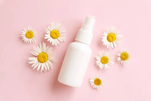Mockup white cosmetic spray mini travel bottle and blooming medical chamomile Daisy on pink background. Body mist, sanitizer, perfume, sunscreen oil, deodorant. Front view, blank bottle, template.