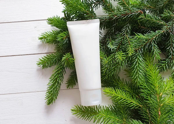White squeeze cosmetic cream tube and green fir tree on white wooden background. Mockup moisturizer blank bottle branding, toothpaste, skincare, cleanser, makeup removal, gel, shampoo pack, lube
