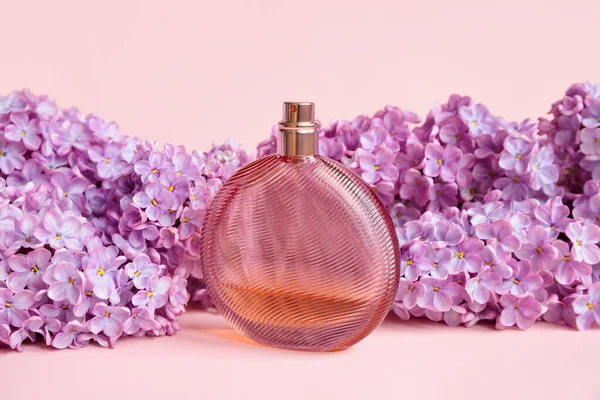 Perfume spray bottle, pink lilac flowers a lot on pink background. Transparent unbranded brown glass perfume bottle for branding and label. Eau de toilette. Mockup, spring.