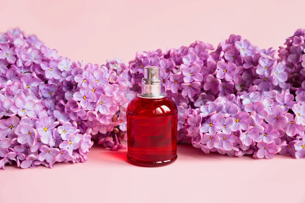 Perfume spray red bottle, lilac flowers on pink background. Eau de toilette, front view, mockup. Home perfume.