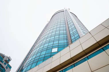 Gökdelen cephesinde beyaz yağmur bulutlarının arkasında mavi cam pencereler var. Aşağıdan bak, perspektiften bak. Astana Nur-Sultan, Kazakistan - 10.24.2022.