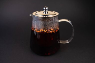 Siyah arka planda deniz dikenli üzümlü, sıcak meyve siyah çayla şeffaf çaydanlık..