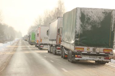 KRASLAVA DISTRICT, LATVIA - 1 Aralık 2023: Letonya-Belarus sınırındaki yük kamyonları kontrol noktası Paternieki 'den önce. Araçlar dondurucu soğukta karla kaplı bir yolda duruyorlar.