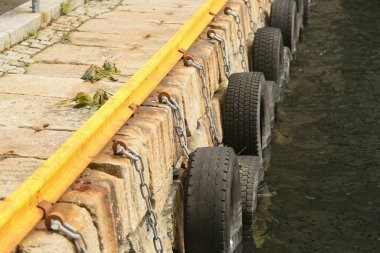 Pier lined with tires as fenders for the boats docking on them clipart