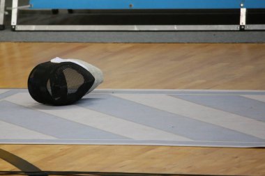 Spor salonunun ahşap zemininde duran eskrim maskesi eğitim ve eskrim yarışmasının sembolü.