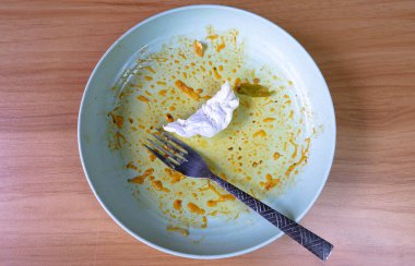 Bitmiş ya da yarım kalmış çatallı ve kullanılmış peçeteli bir tabağın üst görünümü.