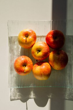 Şeffaf bir tabakta bir çift elma. Elmalar sarı-kırmızıdır. Sert ışık.