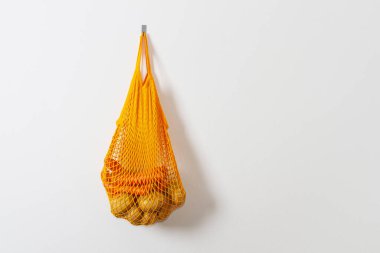 mesh grocery bag. Reusable bag. Vegetarianism, raw food diet, conscious consumption, grid. orange mesh bag hanging on a hook. Potato bag. Raw potatoes.
