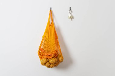 mesh grocery bag. Reusable bag. Vegetarianism, raw food diet, conscious consumption, grid. orange mesh bag hanging on a hook. Potato bag. Raw potatoes.