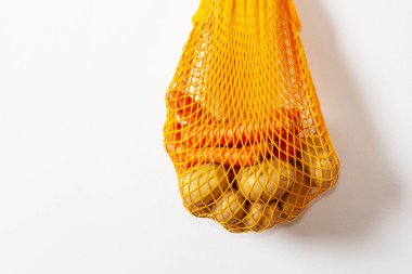 mesh grocery bag. Reusable bag. Vegetarianism, raw food diet, conscious consumption, grid. orange mesh bag hanging on a hook. Potato bag. Raw potatoes.