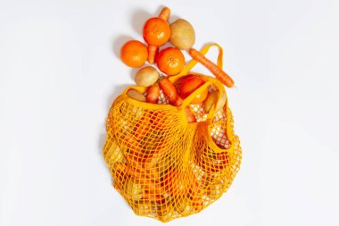 Orange mesh bag. View from above. Close-up. Fresh vegetables from the farmers market. Raw potatoes, raw carrots. Conscious consumption, reusable bag, string bag. Vegetarianism, raw food diet, ecology, fresh vegetables. On a white background.