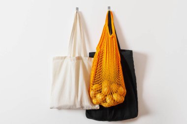 mesh grocery bag. Reusable bag. Vegetarianism, raw food diet, conscious consumption, grid. orange mesh bag hanging on a hook. Several shopping bags. White, black, yellow. Raw potatoes