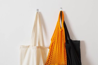 mesh grocery bag. Close-up of bag handles. Reusable bag. Vegetarianism, raw food diet, conscious consumption, grid. orange mesh bag hanging on a hook. Several shopping bags. Black, yellow, white