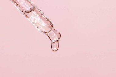 Sıvı damlayan kozmetik pipeti ve pembe arka plan, serum, serum, jel, vitamin, su, yağ damlaları