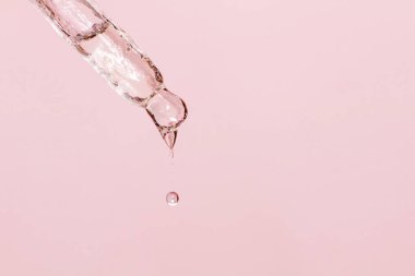 Sıvı damlayan kozmetik pipeti ve pembe arka plan, serum, serum, jel, vitamin, su, yağ damlaları