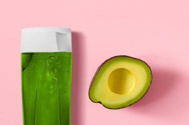 Pembe avokado arka planında şeffaf bir kozmetik şişede yeşil jel. Avokado şişenin yanına yakın çekim yaptı. Avokado kozmetikleri.