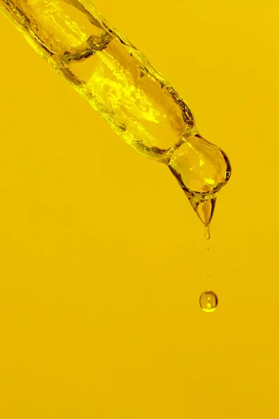 Cosmetic pipette with dripping liquid, oil and drops on a yellow background, serum, serum, gel, vitamin, water, oil