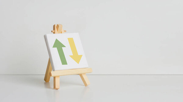 Mini painting on an easel on a light background. With drawn arrow up and down. Symbol of growth and decline