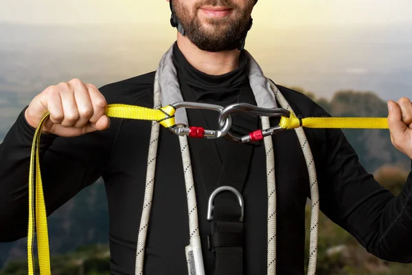 A man in climbing equipment holds carbines. Shows the attachment of equipment. In the mountains. Alpinism, high-rise works, industrial mountaineering. On high.
