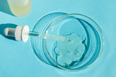 Petri kabı. Şeffaf jelle. Bir pipetle. Kozmetik şişesi. Mavi bir arkaplanda.