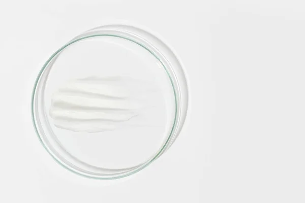 Hafif arka planda bir petri kabı. Beyaz krema lekesi de var. Kozmetik krem, yüz maskesi, krem deseni. Yukarıdan görüntüle