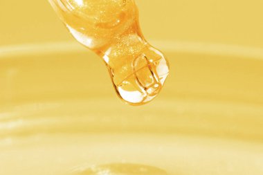 Damlayan sarı sıvılı boru. Ya da sıvı altın. Yakın plan. Altın bir arka planda. Laboratuvar, kimya, tıp. Kozmetik araştırması. Parla.